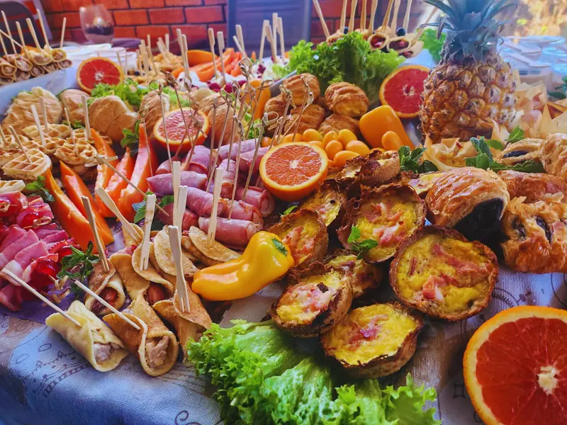 A colourful Deli-icious! harvest table with quiches, wraps, cold meats, fresh fruit and peppers